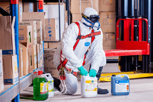 A worker in a hazmat suit handling bottles of chemicals in a warehouse. 